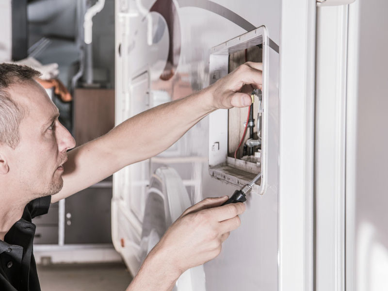 Caucasian RV Repair Technician in his 40s Looking For Potential Problem Inside Travel Trailer Propane Gas Heating System Compartment.