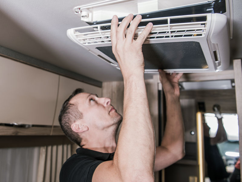 Caucasian RV Appliances Technician in His 40s at Work. Looking For Potential Issue with Air Condition Unit Inside Motorhome. RV Industry Theme.