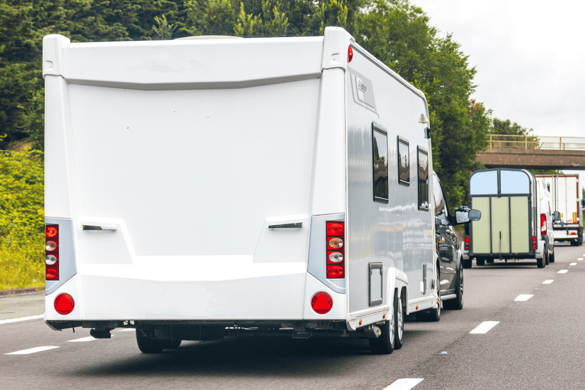 A white caravan is being towed on a UK motorway, with vehicles and greenery visible in the background.