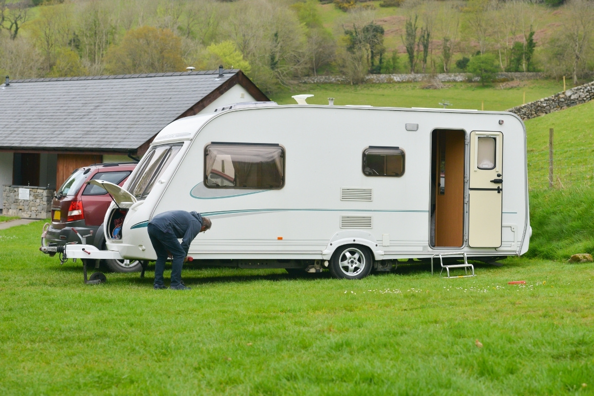 A man is inspecting his caravan at a campsite, ensuring it is in good condition for use.