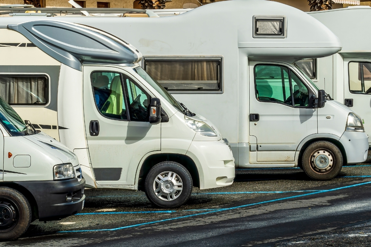 A row of motorhomes parked neatly in a spacious parking lot under clear blue skies.