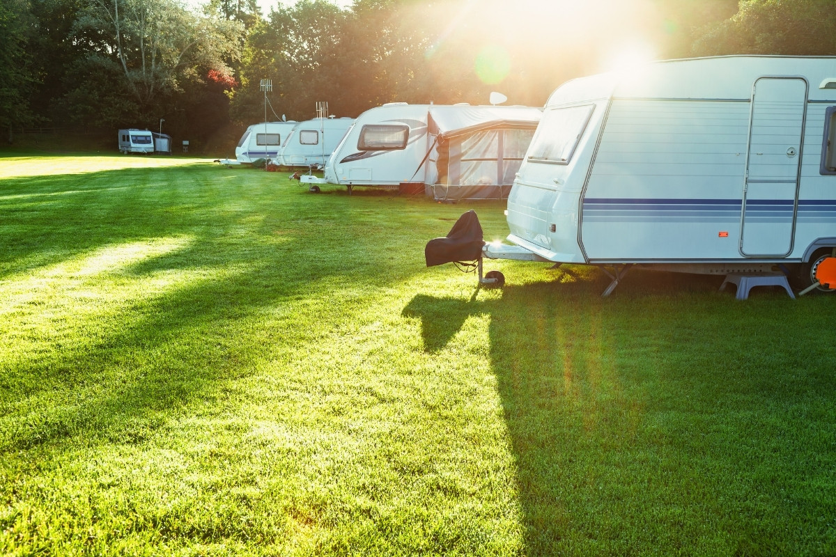 A group of caravans parked in a sunny UK campsite, surrounded by green grass and trees.
